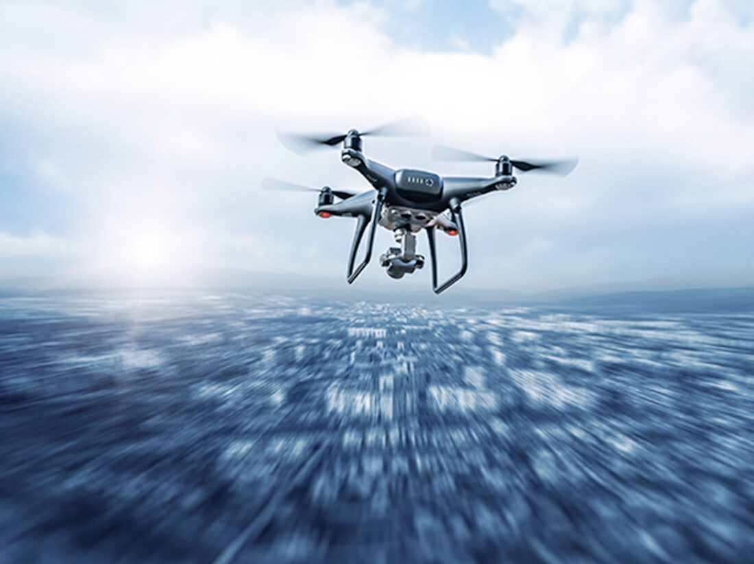 海上を飛行するドローン。青い海面の上空を飛ぶ四葉のプロペラを持つ黒いドローン。カメラ付きで、海面が動きのあるブラー効果で表現されている。